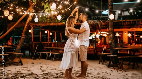 Couple dances on beach at night under string lights near a bar with palm trees