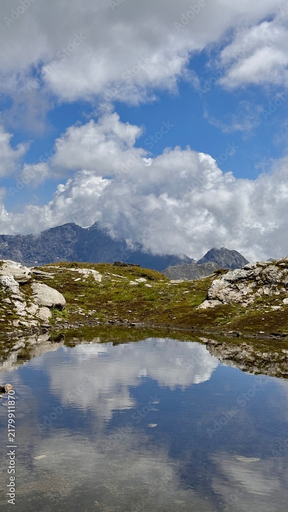 Fototapeta premium Mountains reflected in a calm pond during daytime with clouds and blue sky
