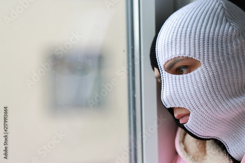 Obraz na płótnie Man wearing a black and white knitted balaclava mask looking through a window