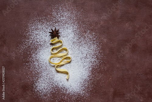 Raw yellow italian pasta (nests) pappardelle, fettuccine or tagliatelle in the shape of a Christmas tree on a brown background, close up. Egg homemade noodles cooking process,festive mood.