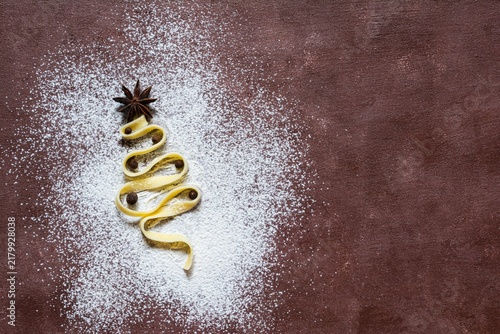 Raw yellow italian pasta (nests) pappardelle, fettuccine or tagliatelle in the shape of a Christmas tree on a brown background, close up. Egg homemade noodles cooking process,festive mood.