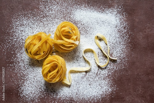 Raw yellow italian pasta (nests) pappardelle, fettuccine or tagliatelle on a brown background, close up. Egg homemade noodles cooking process, festive mood.