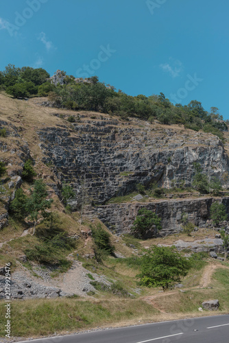 Foto Layered limestone cliff with a scree cone and footpath above the road through Cheddar Gorge, tree line along the top