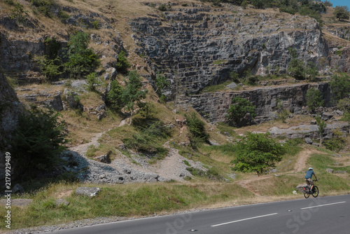 Obraz na plátne A cyclist appears tiny on the road through Cheddar Gorge below a huge layered rock face and a scree slope