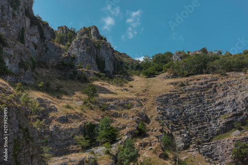 Fotografía Dry valley of grass climbing between limestone crags at Cheddar Gorge, with stacked rock beds on both flanks