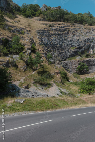 Canvas Print Winding road at the foot of a limestone cliff in Cheddar Gorge, with birch saplings clinging to the slope