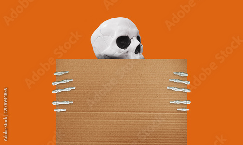 White skull and skeleton hands holding a blank cardboard sign against an orange background