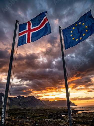 state flag of iceland and flag of european union wave at sunset over mountainous northern terrain reflecting international ties political dialogue and full unity of europe