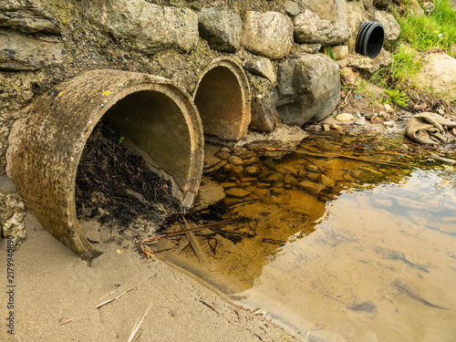 фотографія Two rusty pipes emerge from stone wall, releasing murky brown water