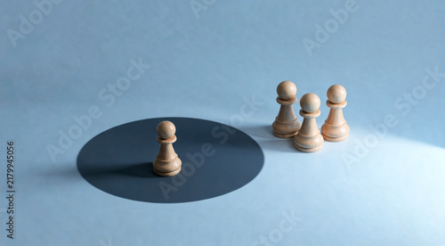 A lone pawn chess piece stands inside a dark circle, separated from three other pawns by a stark blue background