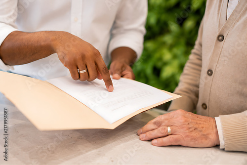  Close-up of customer service rep hands explaining form to elderly customer — silver ring, wedding band, plant wall
