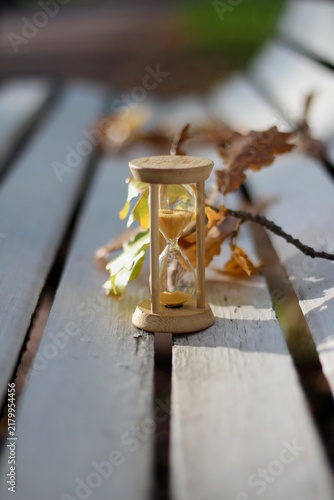 Hourglasses and yellow oak leaves on a white wooden bench — the concept of the changing seasons, a time for rest and walks, leaf fall, the autumn season of life