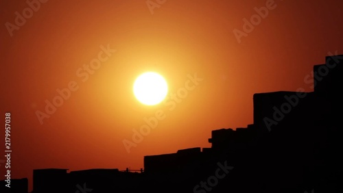 Bild auf Leinwand A brilliant sun on the horizon at sunrise, with the silhouette of dark buildings in the foreground