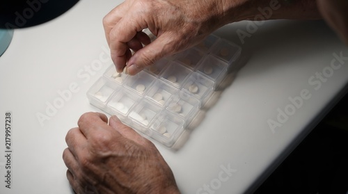 Elderly hands organizing daily pills in plastic organizer