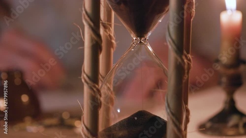 closeup of an antique hourglass with someone writing with a quill pen in the