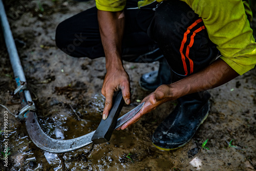 Bild auf Leinwand A worker is manually sharpening a sword with a stone on damp soil in Thailand