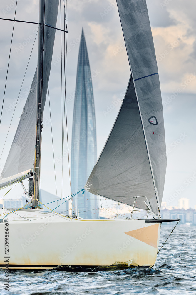 Fototapeta premium sailing regatta in the Gulf of Finland at sunny day, Yachtsmen are sitting amicably on board of the sailing boat, magic splashing water, teamwork, reflections