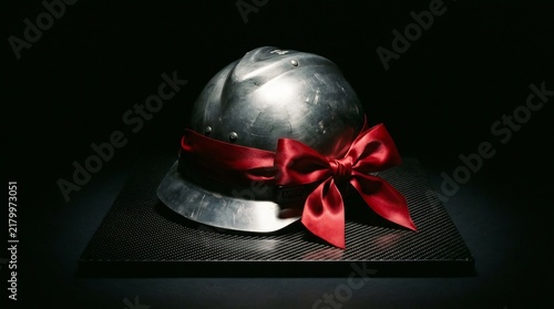 Silver metal hard hat with red satin bow on carbon fiber base. Represents labor appreciation, industrial gift, construction retirement, or safety achievement award.