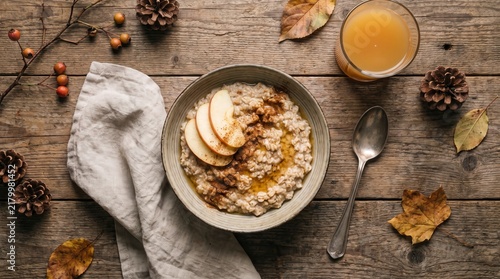 Bowl of oatmeal with apple slices and cinnamon on a rustic wooden table for autumn breakfast