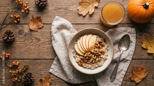 Oatmeal bowl with sliced apples and walnuts on rustic wooden table with autumn decor