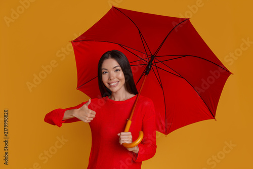 Smiling woman with umbrella giving thumbs up for protection