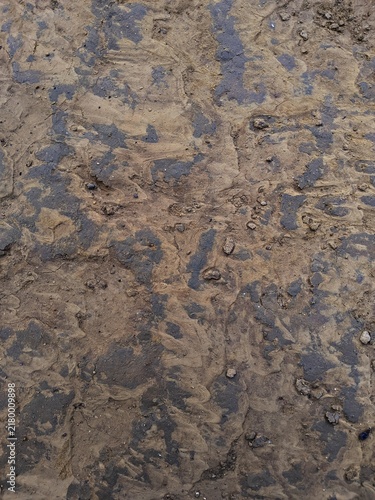 Top view close up background texture of wet muddy ground soil with dark damp patches and rough earthy surface