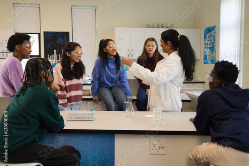 Indian teacher holding blue flask, lab coat teaching teens wearing safety goggles in lab