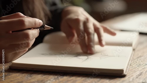 Close up of a person drawing with a pencil in a sketchbook on a wooden table