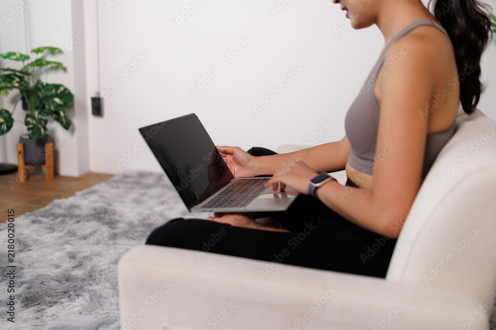 Fototapeta premium Young woman on a sofa using a laptop, focused on remote work or online study in a cozy living room, illustrating a flexible, connected modern lifestyle