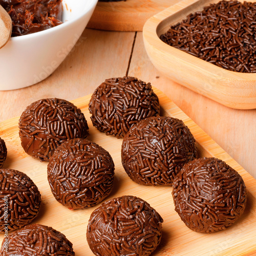 Homemade chocolate brigadeiro coated in sprinkles, presented in a rustic style on a bamboo tray atop a wooden table.