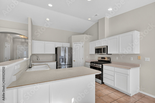 Bright modern kitchen interior with white paneled cabinets, stainless steel refrigerator plus stove