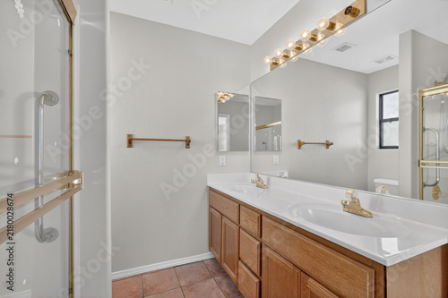 Bathroom with double sink vanity brass fixtures large mirror glass shower light neutral tones