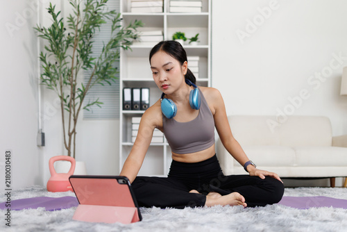Принти на полотні Asian woman exercising at home, watching online fitness class on tablet, staying