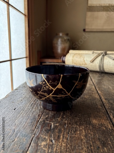 Traditional Japanese black lacquerware bowl repaired with gold kintsugi technique on a rustic wooden table, serene interior with shoji screen and wabi sabi aesthetics