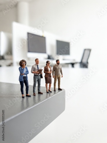 Miniature figures of a diverse business team standing on the edge of a desk in a modern corporate workspace, risk management, business strategy and corporate challenge concept