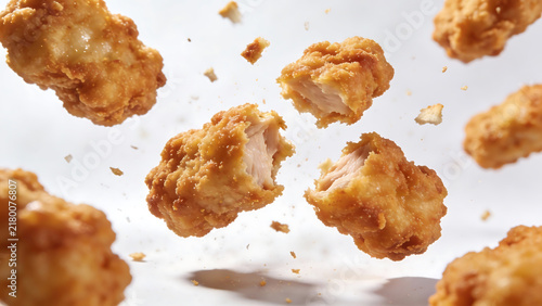 Crispy chicken nuggets mid-air in slow-motion burst against white background with crumbs scattering