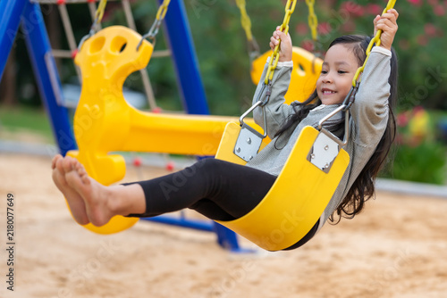 happy preschool child girl swinging on swing set at outdoor playground