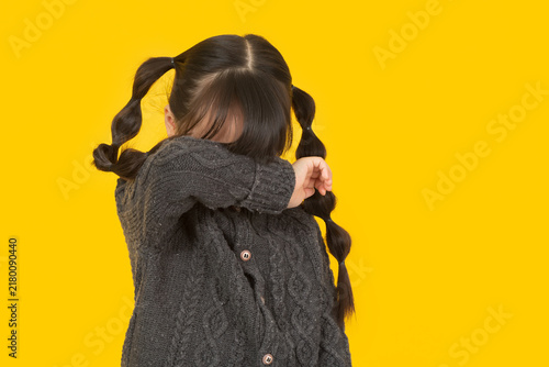 Quadro su tela Shy little girl wearing a grey cardigan and hiding her face behind her arm