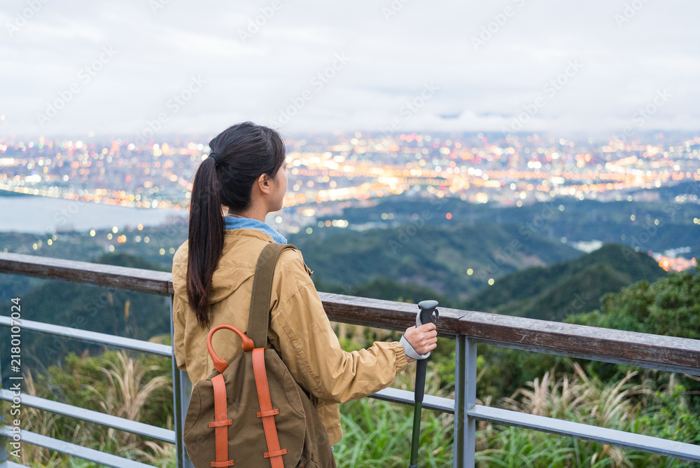 Obraz premium Profile view of female hiker holding trekking poles looking at Taipei view
