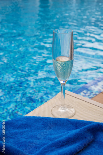 A glass of champagne and a blue towel by a swimming pool.
