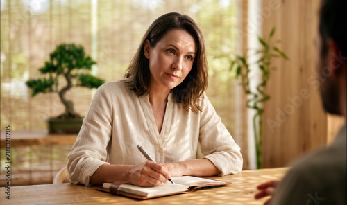 Professional woman writing notes and listening intently during meeting in modern office, business consulting or therapy.