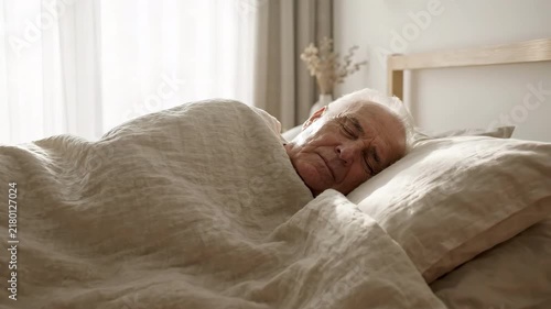 Elderly senior man sleeping peacefully in cozy bed covered with warm blanket, peaceful morning in light bedroom interior, healthy rest, deep sleep quality, aging care, domestic lifestyle concept shot