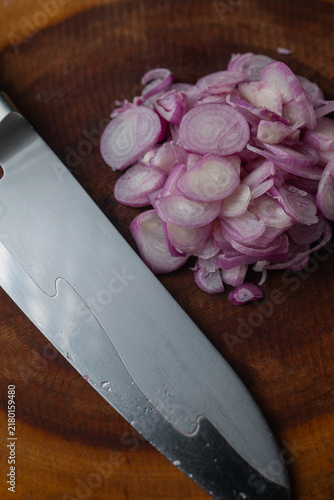 Foto Vertical close up of chef knife blade beside sliced purple shallots on wooden board