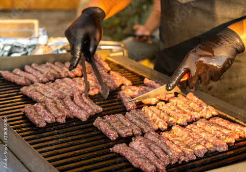 Traditional Balkan cevapi made from minced meat being grilled on a hot barbecue. Close-up of a cook preparing cevapi at an outdoor food stall.