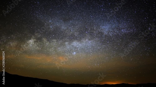 Milky way galaxy moving across the starry night sky with mountain silhouettes and light pollution on the horizon.