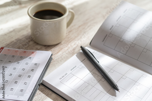 Fotografie Desk setup showing an open planner, calendar, pen, and a cup of coffee, represen