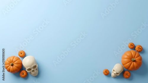 Top view of human skulls and orange pumpkins arranged on a light blue background for halloween