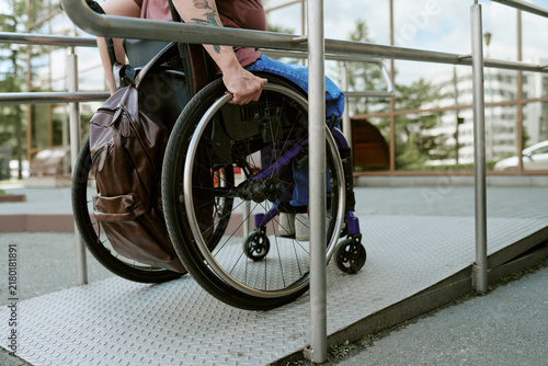 Fotografie Caucasian woman with disability moving up wheelchair accessible ramp outdoors near modern building