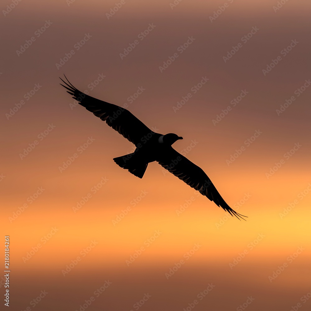 Naklejka premium Majestic black bird gliding through a warm orange sunset sky with outstretched wings, creating a dramatic silhouette of freedom