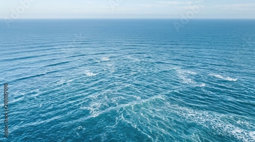 Waves roll across a vast expanse of deep blue ocean. Sunlight reflects off the water, creating white foam and ripples.